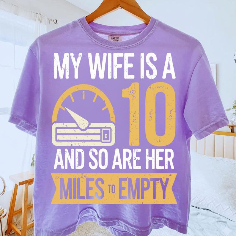 May include: A lilac t-shirt with the text "MY WIFE IS A 10 AND SO ARE HER MILES TO EMPTY" in white and yellow. The design includes a speedometer graphic.