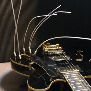 May include: A black electric guitar with gold hardware and a cream-coloured binding. The guitar has a hollow body and a single cutaway. There are several clear plastic cable ties attached to the guitar.