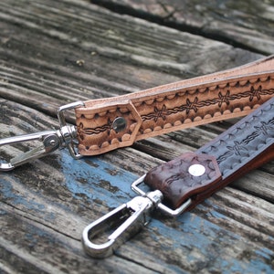 May include: Two leather keychains with a barbed wire design. One is brown and the other is light brown. Both have silver clasps.