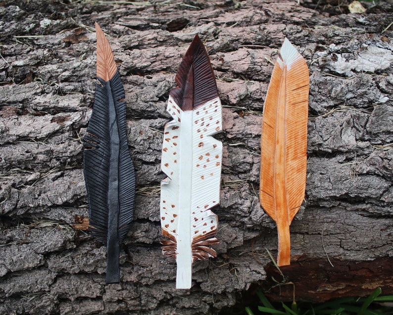 Puede incluir: Tres plumas de cuero, cada una con un color y un patr&oacute;n diferente. Las plumas son negras con puntas marrones, blancas con manchas marrones y negras, y marrones con rayas blancas.