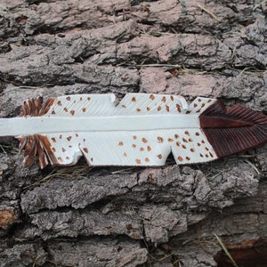 Puede incluir: Una pluma de madera blanca y marr&oacute;n con manchas marrones. La pluma est&aacute; tallada y pintada.