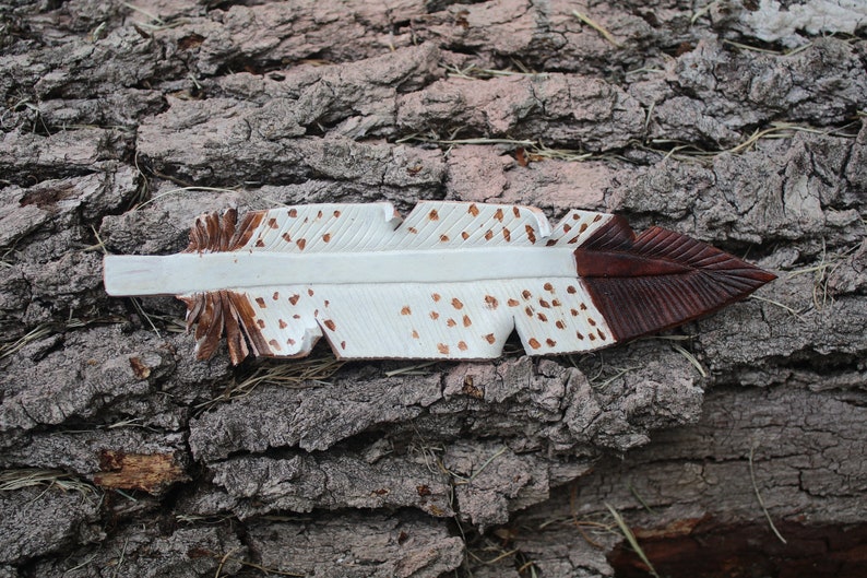 Puede incluir: Una pluma de madera blanca y marr&oacute;n con manchas marrones. La pluma est&aacute; tallada y pintada.