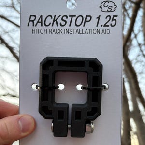 Puede incluir: Ayuda de instalaci&oacute;n de portaequipajes Rackstop 1.25 negro sobre una tarjeta blanca. El texto en la tarjeta dice "Effortless Pin Alignment Every Time" y "For 1.25in Receiver Hitch Systems". El producto est&aacute; dise&ntilde;ado para ayudar con la instalaci&oacute;n del portaequipajes.