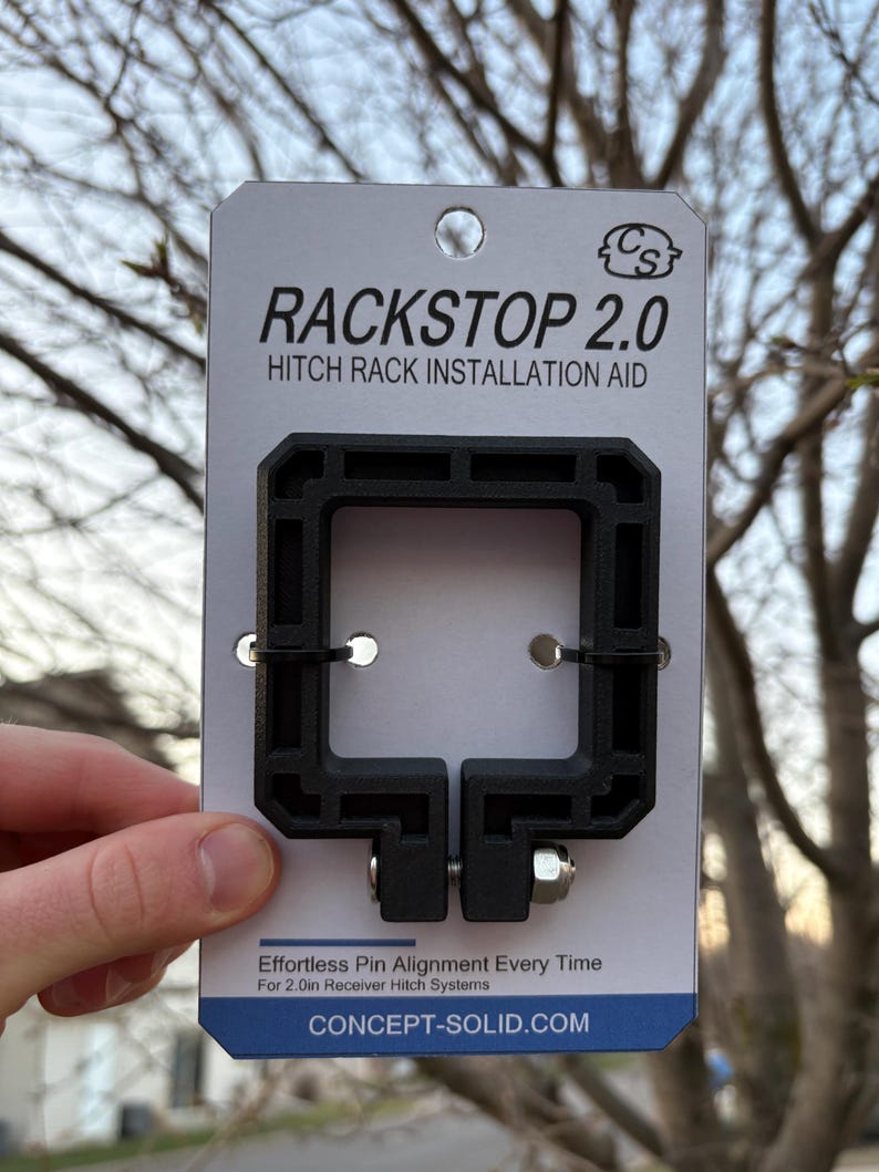 Puede incluir: Ayuda de instalaci&oacute;n de portaequipajes de enganche Rackstop 2.0 negro. El producto est&aacute; sostenido por una mano. El producto es un cuadrado negro con un perno y el texto "Effortless Pin Alignment Every Time" y "CONCEPT-SOLID.COM".