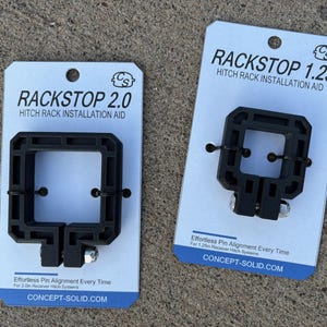 Puede incluir: Dos ayudas de instalaci&oacute;n de portabicicletas negras, etiquetadas como "RACKSTOP 2.0" y "RACKSTOP 1.25", se muestran en tarjetas blancas. Las ayudas tienen un dise&ntilde;o cuadrado con una abertura central y est&aacute;n dise&ntilde;adas para una alineaci&oacute;n sencilla de los pasadores. Las tarjetas incluyen el sitio web CONCEPT-SOLID.COM.