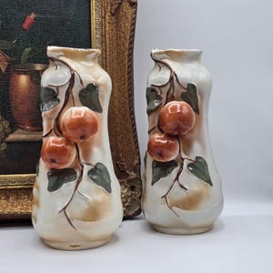May include: A pair of vintage ceramic vases with a white background and a design of orange fruit and green leaves.