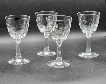 Puede incluir: Cuatro copas de vino de cristal transparente con diseños florales grabados. Las copas tienen un diseño clásico con base de tallo y cuenco redondeado. Las copas se muestran sobre una superficie oscura.