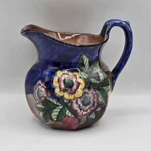 May include: A blue and brown ceramic pitcher with a floral design. The pitcher has a wide mouth and a handle. The flowers are yellow, pink, and red.