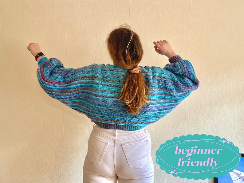 May include: A cropped, multi-colored sweater with blue, purple, and gray horizontal stripes. The sweater has long, voluminous sleeves and a ribbed hem. The text "beginner friendly" is in a teal oval. The model is wearing white jeans.