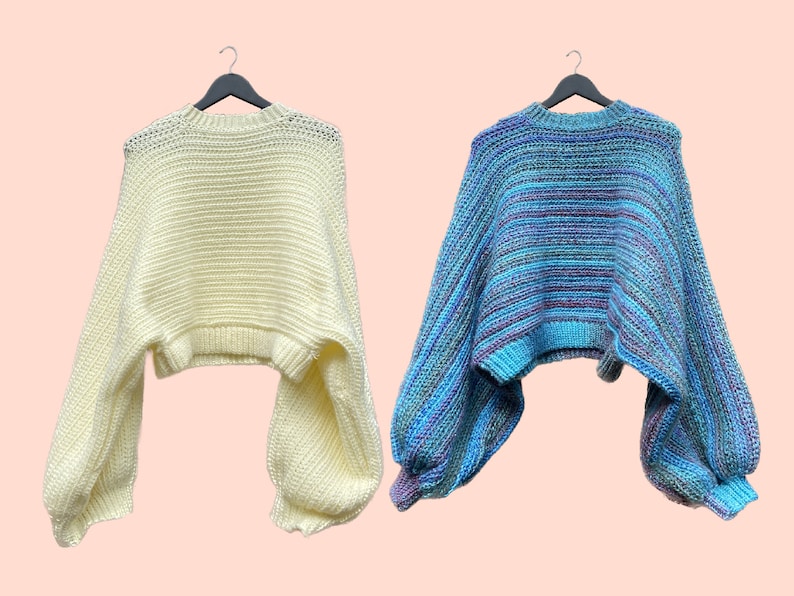 May include: Two sweaters on black hangers. One is a pale yellow with long, voluminous sleeves. The other is a blue sweater with horizontal stripes of various shades of blue, purple, and teal, also with long, voluminous sleeves. Both sweaters have a cropped design.