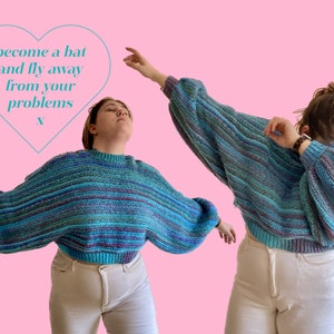 May include: Two people wearing a blue, teal, and purple striped sweater with balloon sleeves and a ribbed hem. The text "become a bat and fly away from your problems" is inside a heart shape. The background is pink.