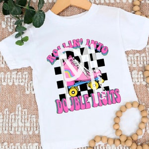 May include: White t-shirt with a pink roller skate graphic and the text "Rollin' into double digits" in a retro font.