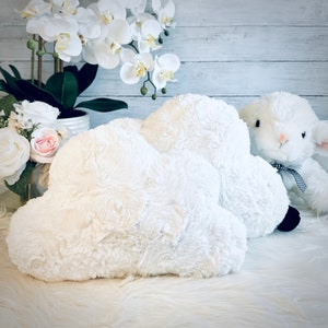 May include: Two white fluffy cloud-shaped pillows with a white fluffy lamb plush toy lying on top of them.