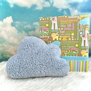 Może przedstawiać: Jasnoniebieska pluszowa zabawka w kształcie chmury z brązowym i ż&oacute;łtym pudełkiem prezentowym z kolorowym wzorem i tekstem "lullaby smile" i "special delivery!"
