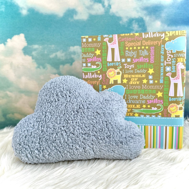 Może przedstawiać: Jasnoniebieska pluszowa zabawka w kształcie chmury z brązowym i ż&oacute;łtym pudełkiem prezentowym z kolorowym wzorem i tekstem "lullaby smile" i "special delivery!"