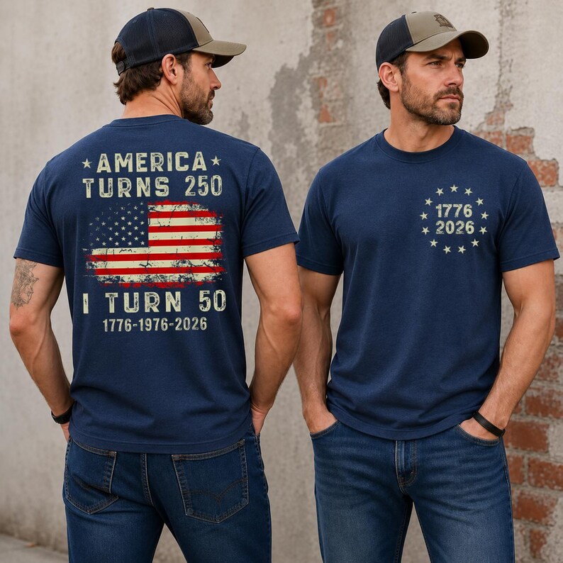 Op de afbeelding: Marineblauwe T-shirts met patriottische ontwerpen. E&eacute;n shirt heeft een versleten Amerikaanse vlag en de tekst "AMERICA TURNS 250" en "I TURN 50 1776-1976-2026." Het andere shirt heeft "1776 2026" omringd door sterren.