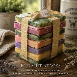 May include: A stack of rectangular soap bars in various colors including green, pink, purple, and yellow, tied together with a yellow and white floral patterned ribbon. The text on the image reads: END CUT STACKS A VARIETY OF SCENTS & COLORS.