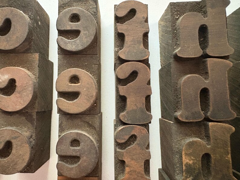 May include: Close-up of vintage wooden printing blocks. The blocks feature the numbers "9", "2", and the letter "h". The blocks are a dark brown color and have a worn, aged appearance. The blocks are arranged in vertical rows.