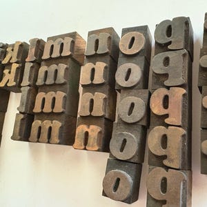 May include: Vintage wooden letterpress printing blocks. The blocks are arranged in rows and columns, displaying the letters "m", "n", "o", "g", and "r". The blocks have a worn, aged appearance with a mix of brown and tan tones.