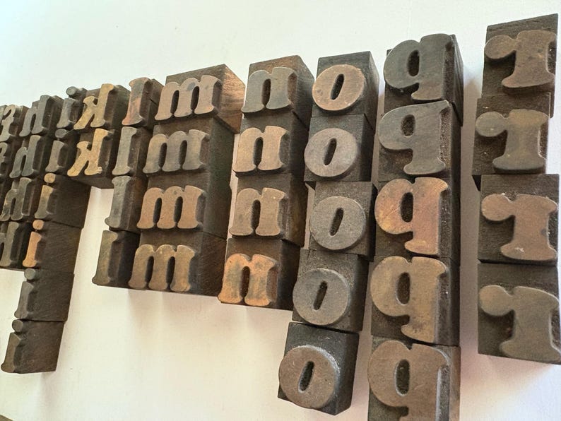 May include: Vintage wooden letterpress printing blocks. The blocks are arranged in rows and columns, displaying the letters "m", "n", "o", "g", and "r". The blocks have a worn, aged appearance with a mix of brown and tan tones.