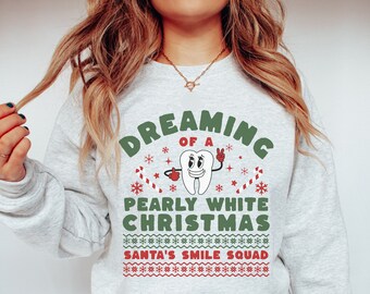 May include: A gray sweatshirt with a green and white design. The design features a cartoon tooth with a peace sign and the text "Dreaming of a Pearly White Christmas Santa's Smile Squad".