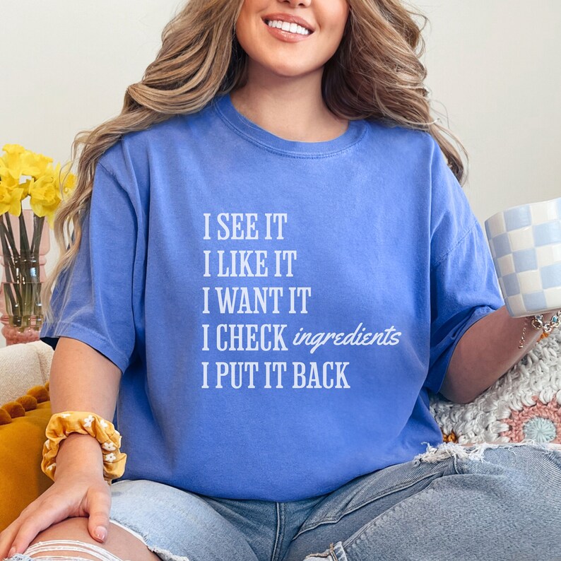 Op de afbeelding: Een lichtblauw T-shirt met de tekst "I see it, I like it, I want it, I check ingredients, I put it back" in wit gedrukt.