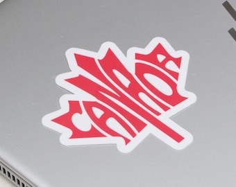 May include: A red and white sticker in the shape of a maple leaf with the word "CANADA" in a stylized font. The sticker is affixed to the lid of a silver laptop.