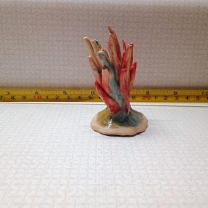 May include: A ceramic coral sculpture with red, blue, and tan hues. The coral is mounted on a round base. The sculpture is approximately 4 inches tall.