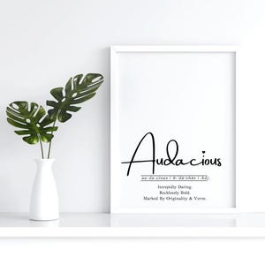 Puede incluir: Impresión enmarcada con la palabra "Audacious" en negro. La definición debajo dice "Intrépido. Audaz. Marcado por la originalidad y el vigor." Un jarrón blanco con hojas verdes está a la izquierda.