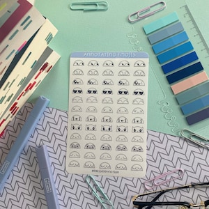 May include: A sheet of stickers with various black and white emoji-style faces. The sheet is on a light blue background with a white border. The text "ANNOTATING EMOJIS" is at the top of the sheet. The text "@DRESSEDINFICTION" is at the bottom of the sheet.
