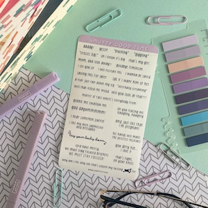May include: A collection of stationery items, including a sticker sheet with phrases, pastel sticky notes, and highlighters. The sticker sheet has the title "SMUTTY GOOD TIME" and various phrases. The background is a mix of light green, gray, and white.