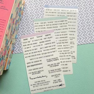 May include: Three rectangular stickers with text, stacked on a light blue surface. The stickers have phrases like "Smutty Good Time" and "I love dilfs." A book with colorful page markers is in the background.