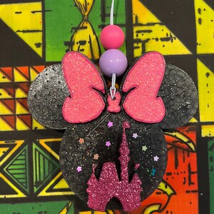 May include: Black glitter Minnie Mouse-shaped ornament with a pink glitter bow and a pink glitter castle. The ornament has a white string with pink and purple beads.