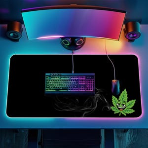 May include: A large rectangular black desk mat featuring a vibrant green cartoon cannabis leaf character with a smiling face. The mat is illuminated by a glowing LED border and sits beneath a computer keyboard, a wired mouse, and a curved monitor.
