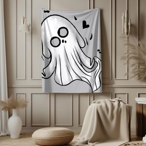 May include: A white ghost illustration with black outlines hangs on a wall. The ghost has large, round eyes and a flowing body. Black hearts and dots are scattered around the ghost. The artwork is displayed on a light gray background.