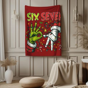 Op de afbeelding: Rode kerstwandtapijt met de woorden "SIX SEVEN" in groen en rood. Het wandtapijt toont twee handen, een groene en een witte, beide met kerstmutsen en kerstverlichting. Zuurstokken en sneeuwvlokken zijn ook aanwezig.