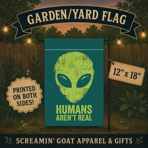 May include: A teal garden flag measuring 12 inches by 18 inches, featuring a distressed lime green alien head graphic and the text "HUMANS AREN'T REAL" in lime green. A tag indicates the design is printed on both sides of the fabric.