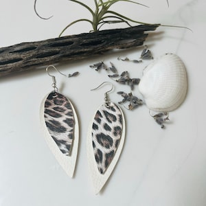 May include: A pair of dangle earrings with a white leather base and a leopard print overlay. The earrings have silver hooks.