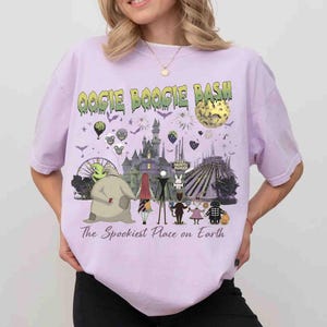 Puede incluir: Una camiseta de color morado claro con un estampado gr&aacute;fico que incluye el texto OOGIE BOOGIE BASH y The Spookiest Place on Earth. El dise&ntilde;o muestra un castillo, una luna, una noria y varios personajes animados en fila.