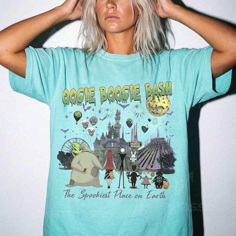 Puede incluir: Una camiseta de color turquesa claro con un estampado gr&aacute;fico que incluye el texto OOGIE BOOGIE BASH y The Spookiest Place on Earth. El dise&ntilde;o muestra varios personajes animados, un castillo, una luna y fuegos artificiales oscuros.