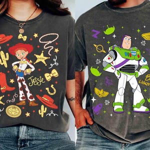 Puede incluir: Dos camisetas gris carbón con personajes de dibujos animados. Una camiseta muestra una vaquera con el nombre "Jessie" y gráficos del oeste. La otra camiseta muestra a Buzz Lightyear con el texto "Buzz Lightyear".