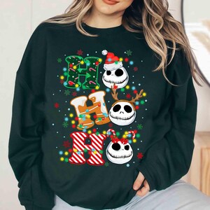 May include: Dark green sweatshirt with the word "HO HO HO" in a festive design. The "H" is decorated with green lights, the "O"s feature Jack Skellington faces, and the "R" is red and white striped. Christmas-themed apparel.