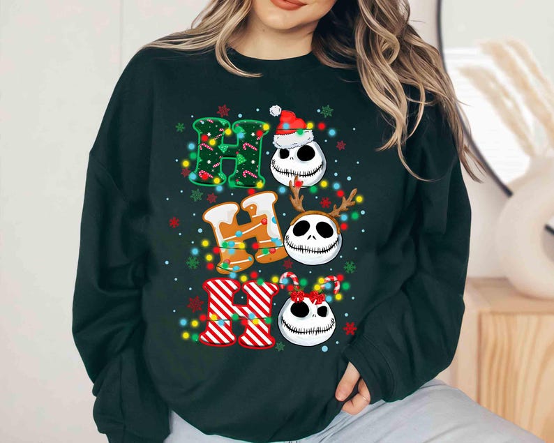 May include: Dark green sweatshirt with the word "HO HO HO" in a festive design. The "H" is decorated with green lights, the "O"s feature Jack Skellington faces, and the "R" is red and white striped. Christmas-themed apparel.