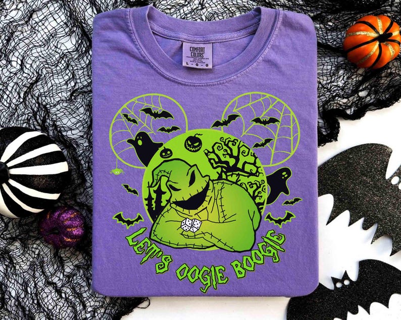 May include: A purple t-shirt featuring a green graphic of a character with dice, bats, and the text "Let's Oogie Boogie". The design includes a green circle with a spiderweb and bats. The shirt is folded on a white surface.