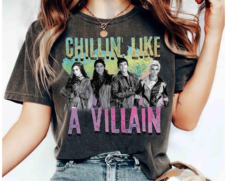 May include: Dark gray t-shirt featuring the phrase "CHILLIN LIKE A VILLAIN" in colorful text above a graphic of four people. The shirt is a comfortable, casual style.