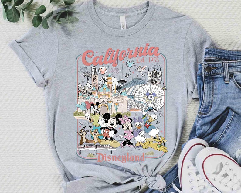 Puede incluir: Camiseta gris con un gr&aacute;fico colorido de Disneyland en California. El dise&ntilde;o incluye a Mickey y Minnie Mouse, y el texto "California Disneyland Est. 1955". La camiseta se combina con vaqueros azules y zapatillas blancas.