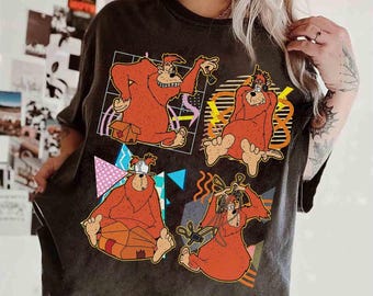 May include: Dark gray t-shirt featuring a cartoon design of four orange bears in various poses. Each bear is set within a geometric frame with colorful accents. The shirt has a vintage, worn look.