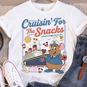 Pode incluir: Camiseta branca com um desenho animado de um capit&atilde;o rato segurando uma bebida e um sorvete. A camisa tem o texto "Cruisin' For The Snacks" em azul e vermelho, com um navio de cruzeiro e outros gr&aacute;ficos.