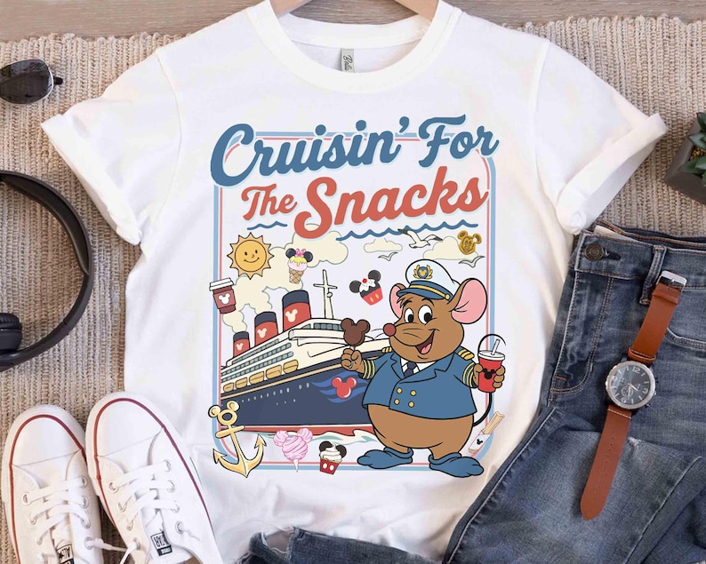 Pode incluir: Camiseta branca com um desenho animado de um capit&atilde;o rato segurando uma bebida e um sorvete. A camisa tem o texto "Cruisin' For The Snacks" em azul e vermelho, com um navio de cruzeiro e outros gr&aacute;ficos.