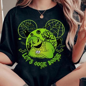 May include: Black t-shirt featuring a green graphic of Oogie Boogie from The Nightmare Before Christmas. The design includes bats, spiderwebs, and the text "Let's Oogie Boogie" in green. The shirt has a round neckline and short sleeves.